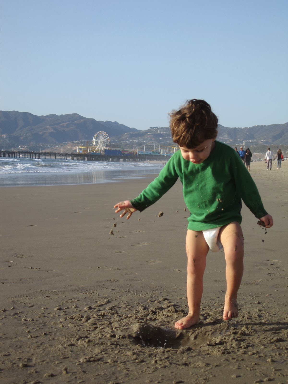 A childhood photo of Samo playing on a beach near a pier.