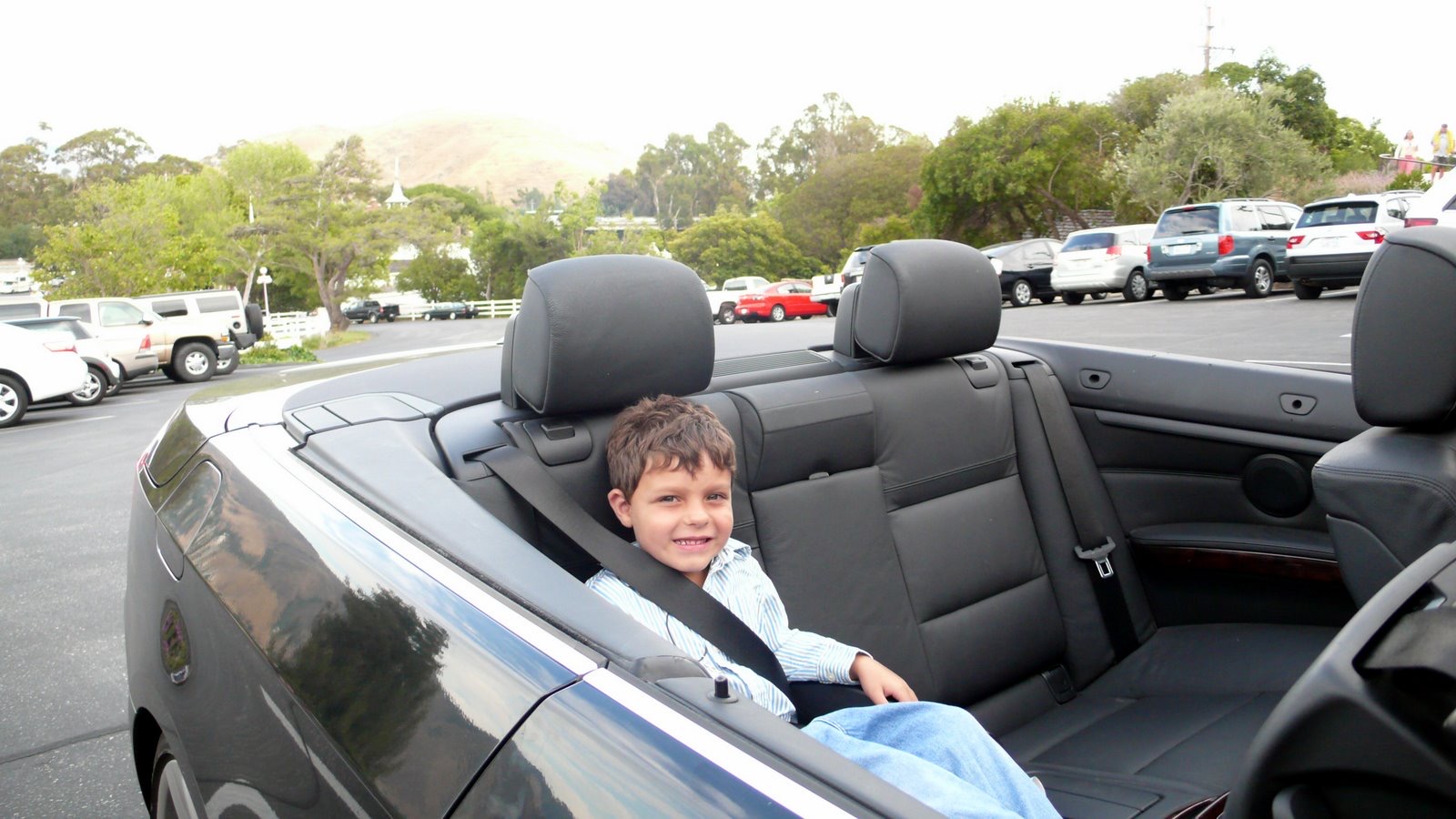 A childhood photo of Samo smiling in the back of a convertible.
